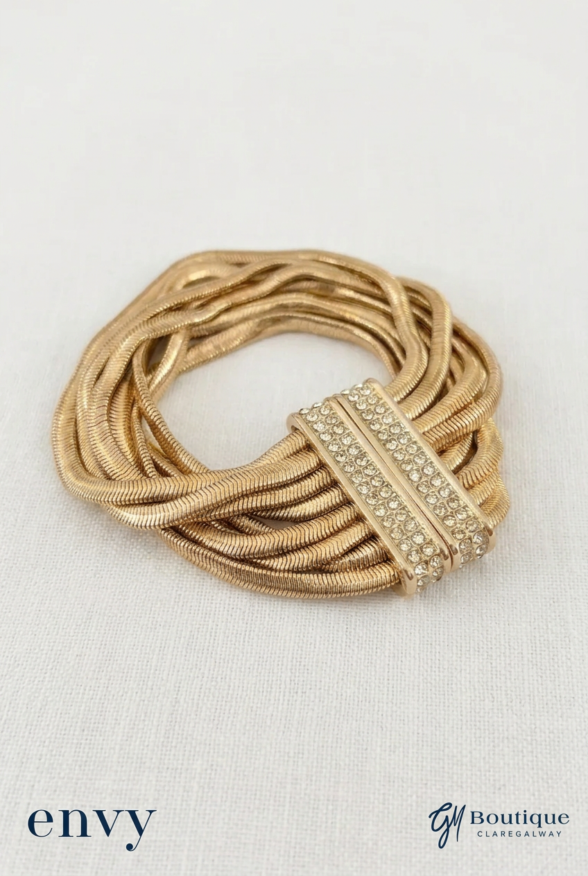 A gold-toned multi-strand snake chain bracelet with a central bar embellished with clear rhinestones, displayed on a textured white fabric background with 'envy' and 'G1 Boutique' watermarks.