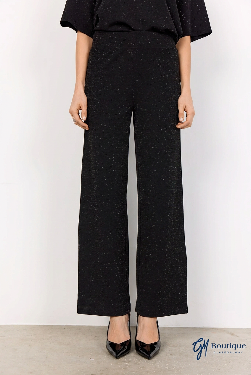 A model wearing black wide-leg cropped trousers with a textured finish, paired with black pointed-toe heels, shown from the waist down against a plain white studio background.
