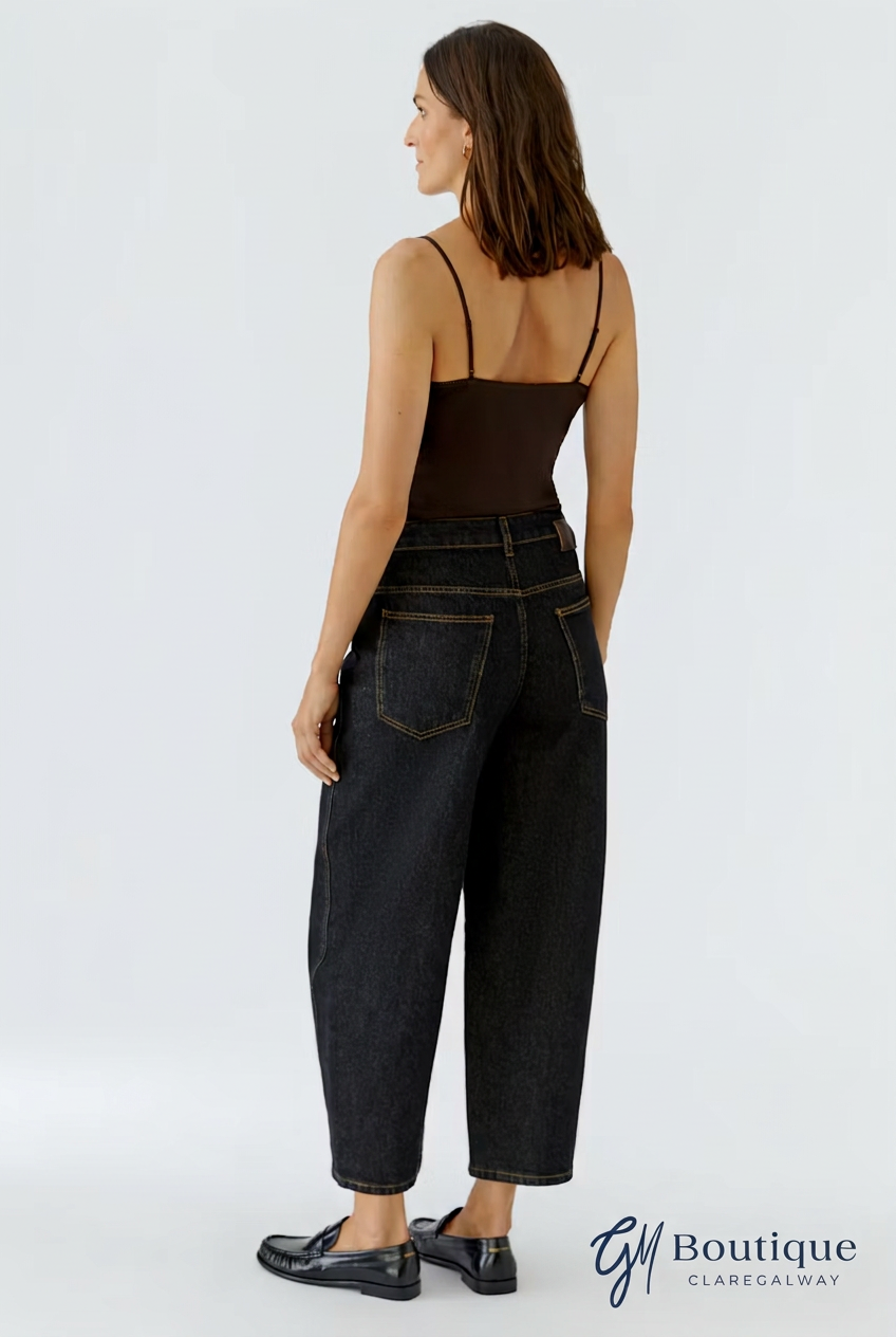 A woman shown from the back wearing a dark brown spaghetti-strap camisole top and dark wash wide-leg cropped jeans, paired with black loafers, against a light gray studio background.
