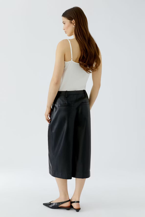 A woman is shown from the back wearing a white spaghetti-strap camisole top and black wide-leg cropped pants, paired with black pointed flat sandals, against a light gray studio background.