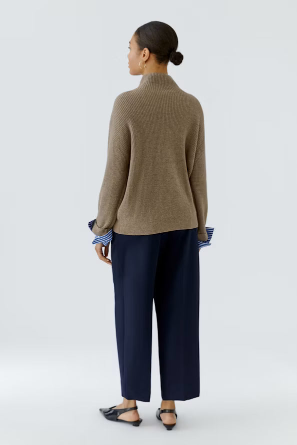 Person wearing a brown sweater and navy pants on a white background