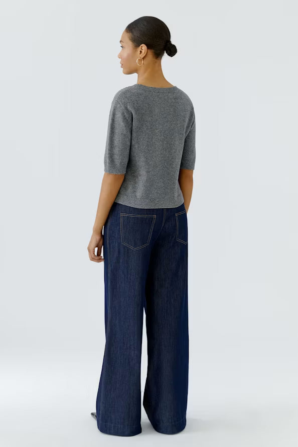 A woman shown from the back wearing a heather gray short-sleeve knit top and dark blue wide-leg denim pants, standing against a light gray studio background.