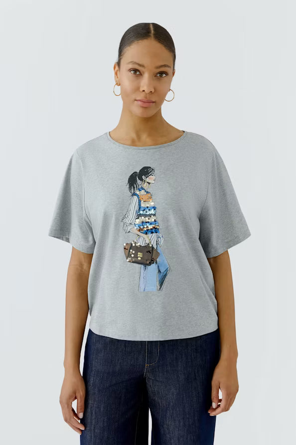 Woman wearing a gray t-shirt with a graphic design on a plain background