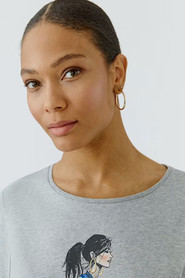 Woman wearing a gray t-shirt with a graphic design on a plain background