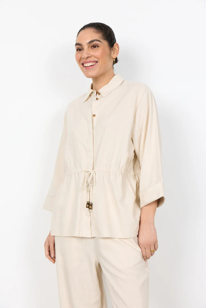 Woman wearing a beige shirt and pants against a white background