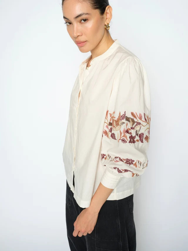 Woman wearing a cream blouse with floral embroidery on a white background