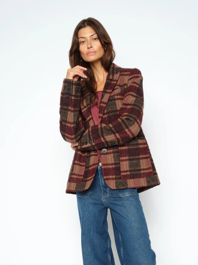 A woman modeling a single-breasted plaid blazer in burgundy, brown, and beige tones, paired with blue jeans, against a plain white studio background.