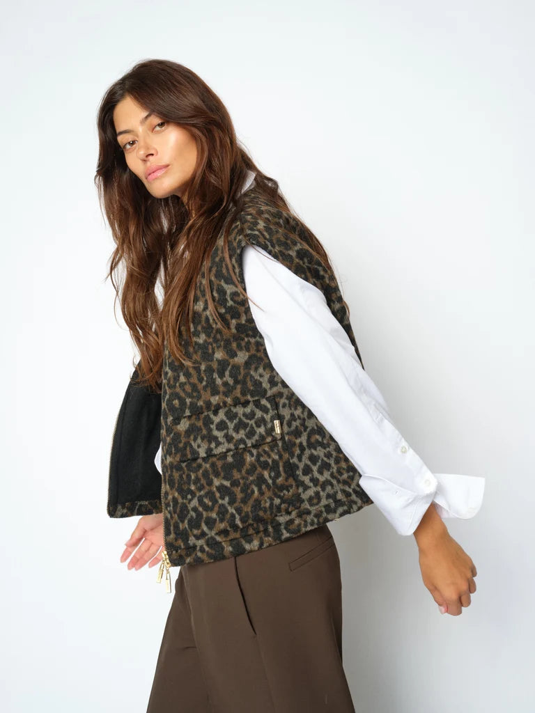 Woman wearing a leopard print vest over a white shirt with a plain background