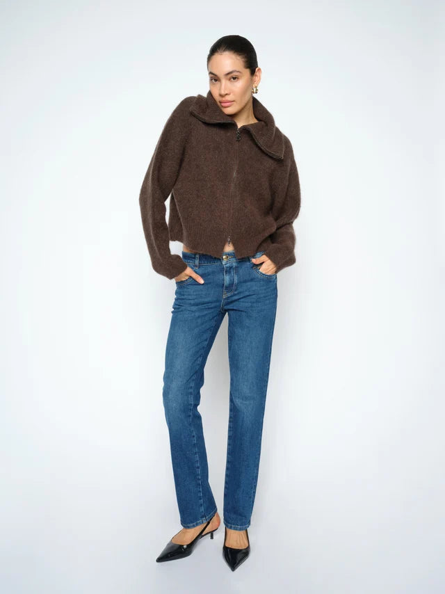 A woman modeling a brown fuzzy cropped sweater with a wide collar, paired with blue jeans and black pointed-toe heels, against a light gray studio background.