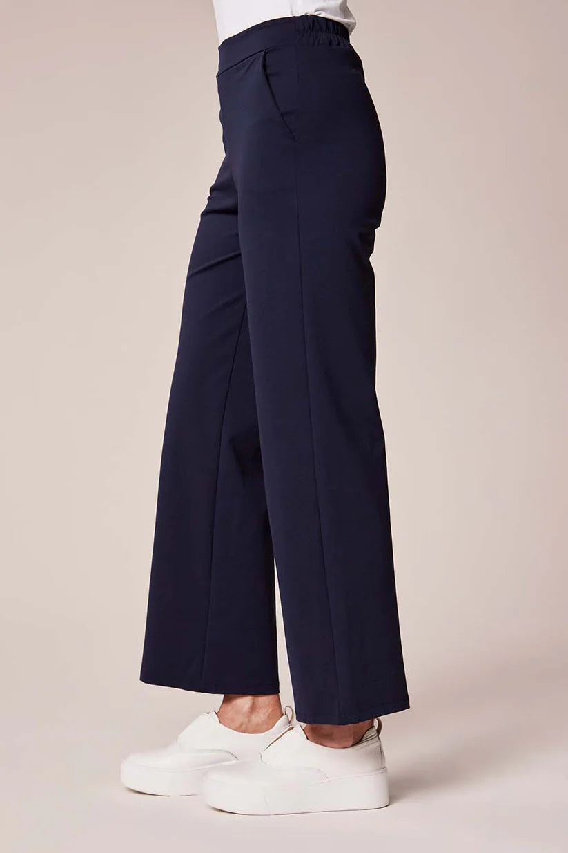 Navy wide-leg pants worn with white sneakers on a beige background