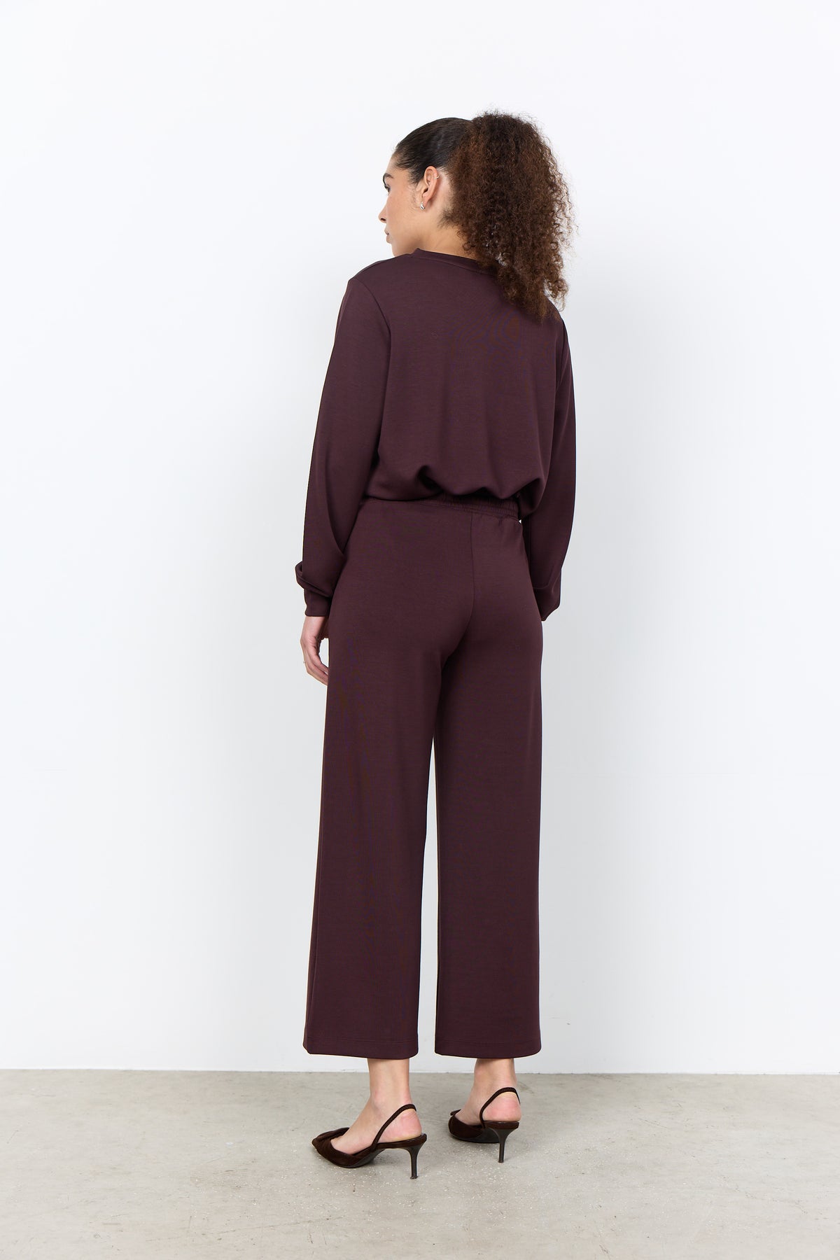 Woman wearing a maroon outfit standing against a white background