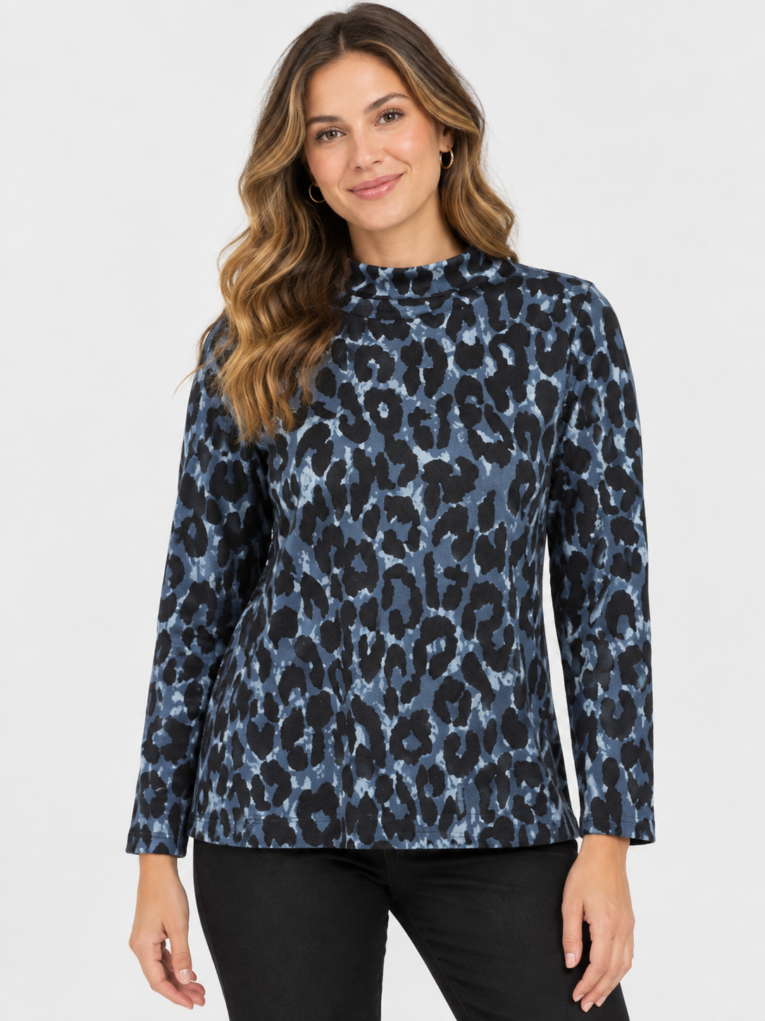 A woman modeling a long-sleeve mock neck top with a blue and black leopard print pattern, paired with black pants, against a light gray studio background.