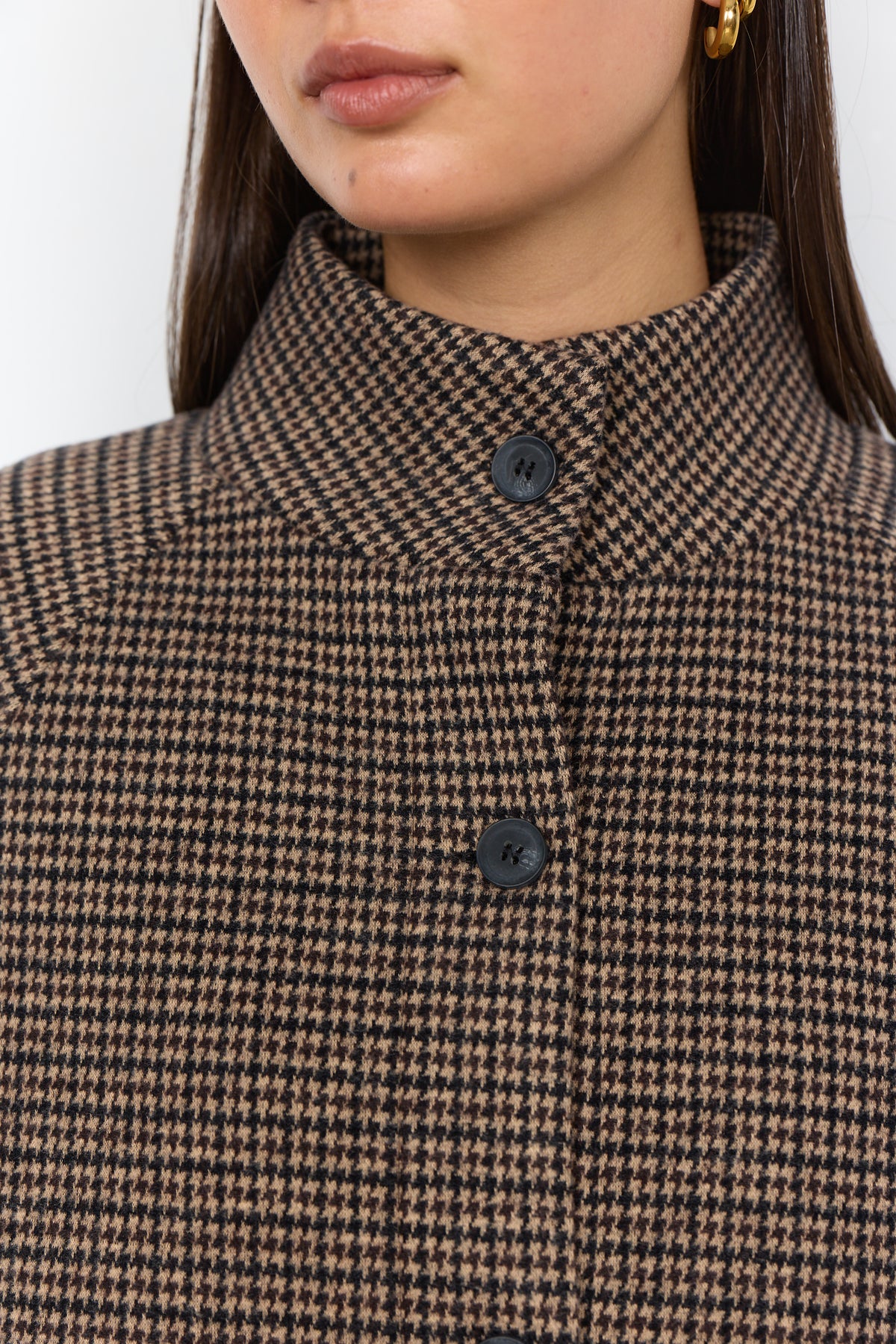 Close-up of a model wearing a brown and black houndstooth patterned coat with a high stand collar and dark buttons.