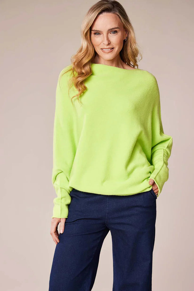 Woman wearing a bright green sweater and blue pants against a beige background