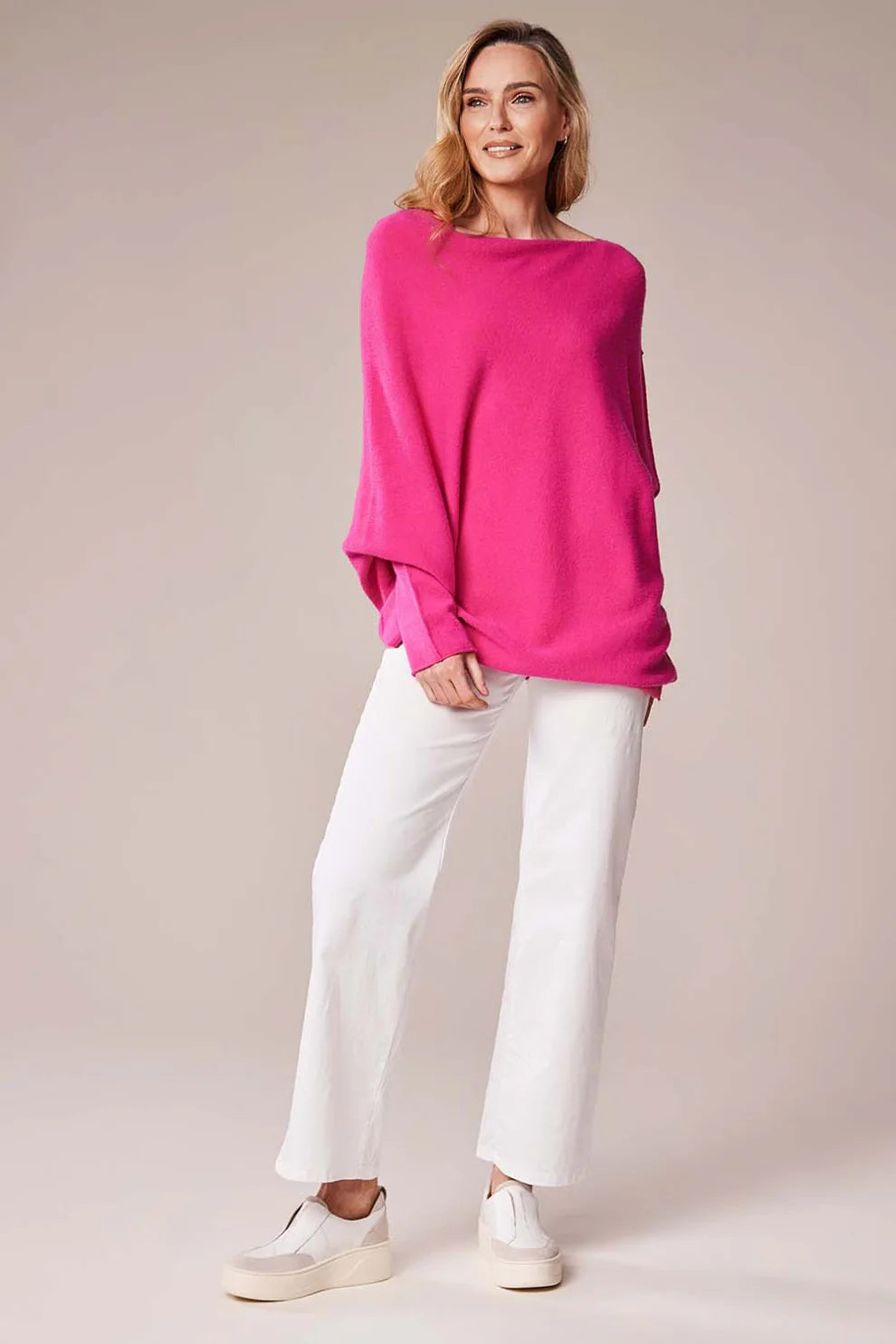 Woman wearing a bright pink sweater and white pants on a beige background