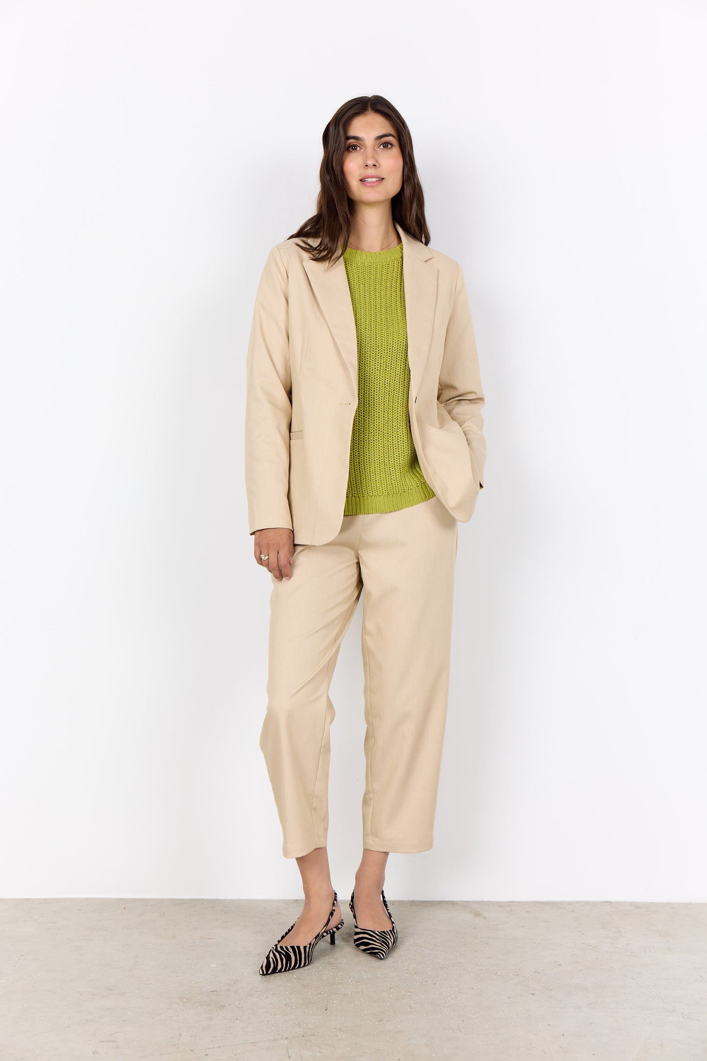 Woman wearing a beige suit with a green top against a white background