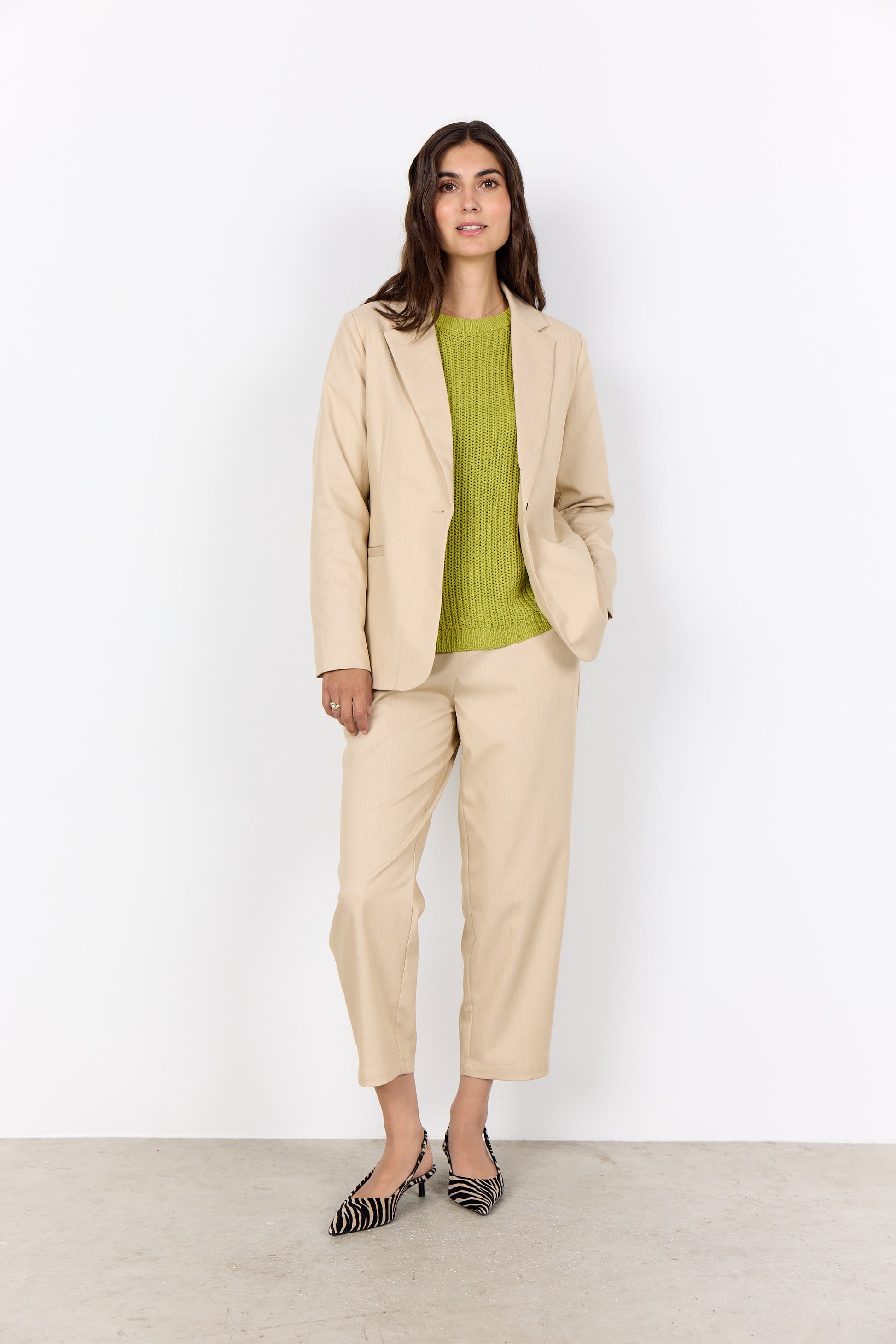 Woman wearing a beige suit with a green top against a white background