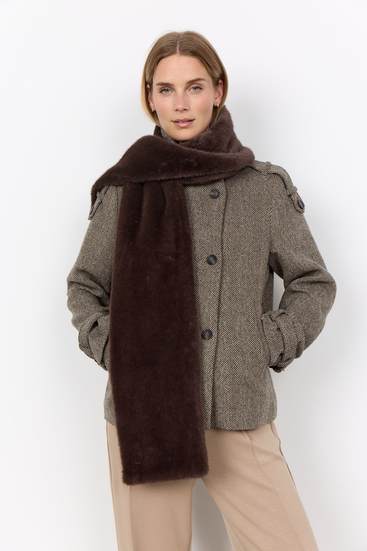 Woman wearing a brown coat with a matching scarf on a white background