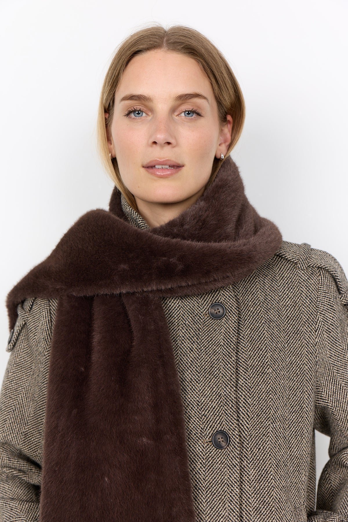 Woman wearing a brown scarf and gray coat against a white background