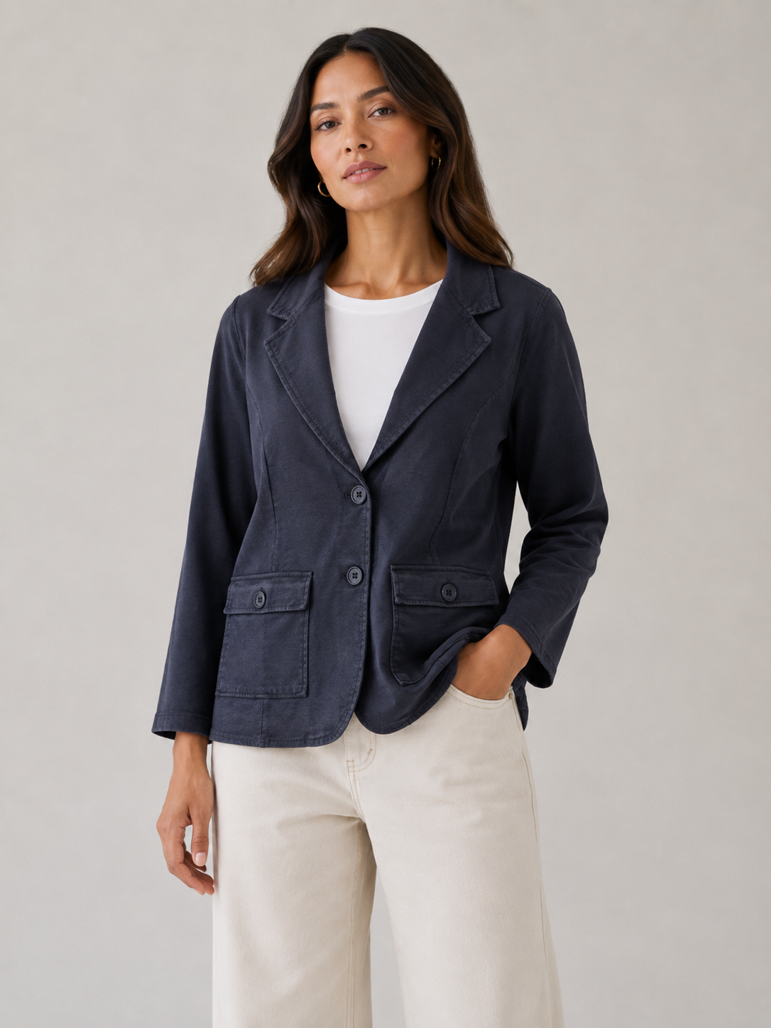 A woman modeling a dark navy blue linen-blend blazer with notch lapels, a two-button front, and two front flap pockets, styled over a white top and cream wide-leg trousers against a neutral studio background.