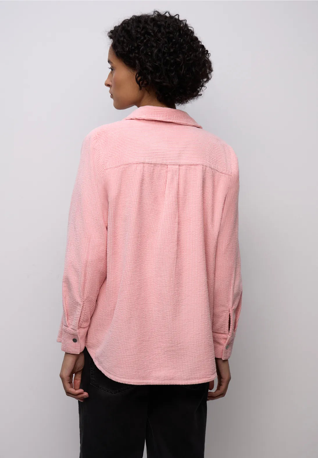 Person wearing a pink shirt against a plain background