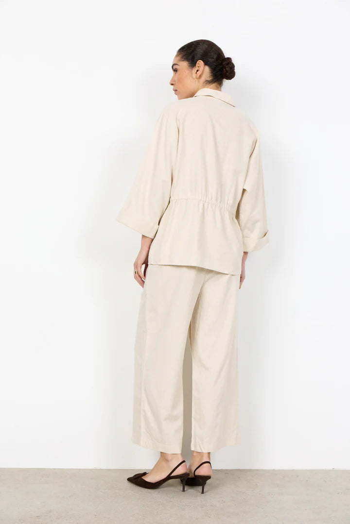 Woman wearing a beige suit standing against a white background