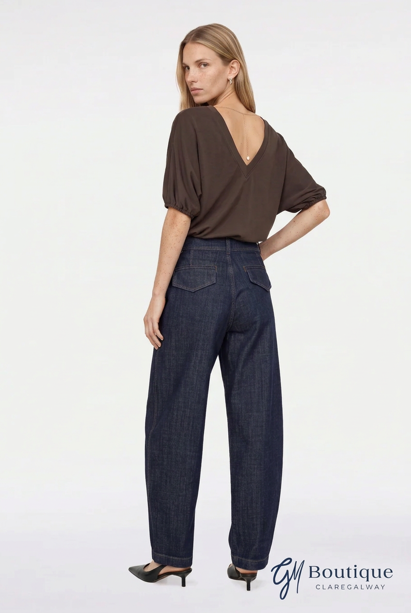 A woman shown from the back wearing a dark brown short-sleeve top and dark blue wide-leg jeans, standing against a plain white studio background. A 'GM Boutique Claregalway' logo is visible in the bottom right corner.