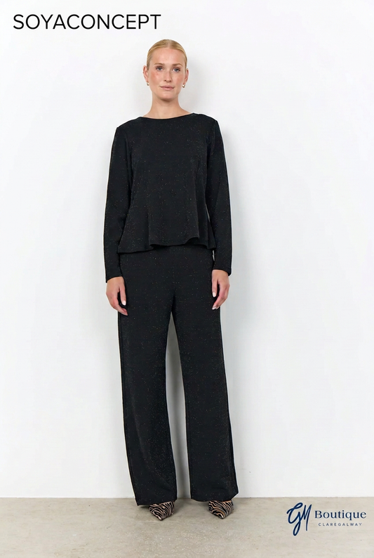 A model stands against a white wall wearing a black long-sleeve top with a peplum-like ruffle and matching black wide-leg trousers. The image has 'SOYACONCEPT' text at the top left and a 'G11 Boutique' watermark at the bottom right.