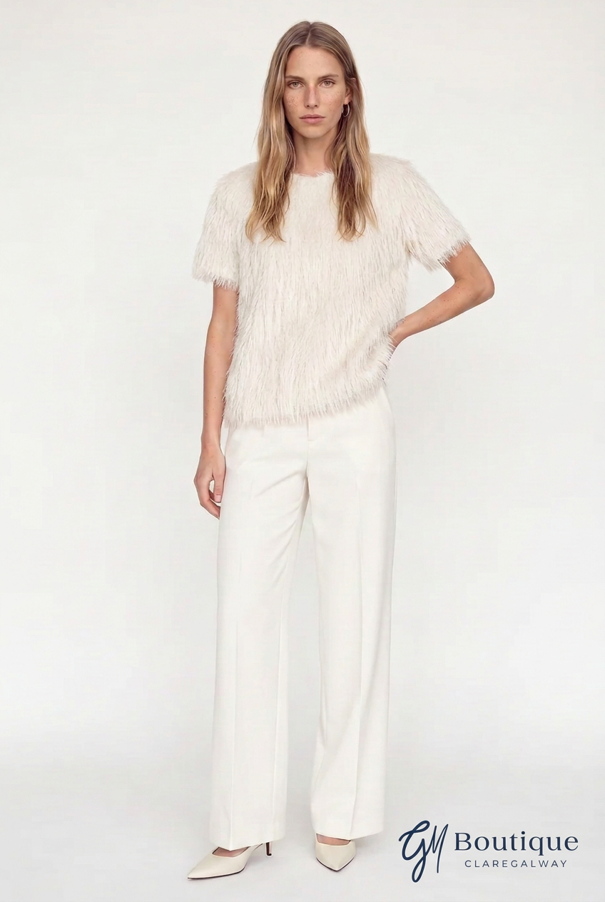 A woman modeling a short-sleeve cream fringed top and matching cream wide-leg trousers against a plain white studio background. A 'GM Boutique Claregalway' logo is visible in the bottom right corner.