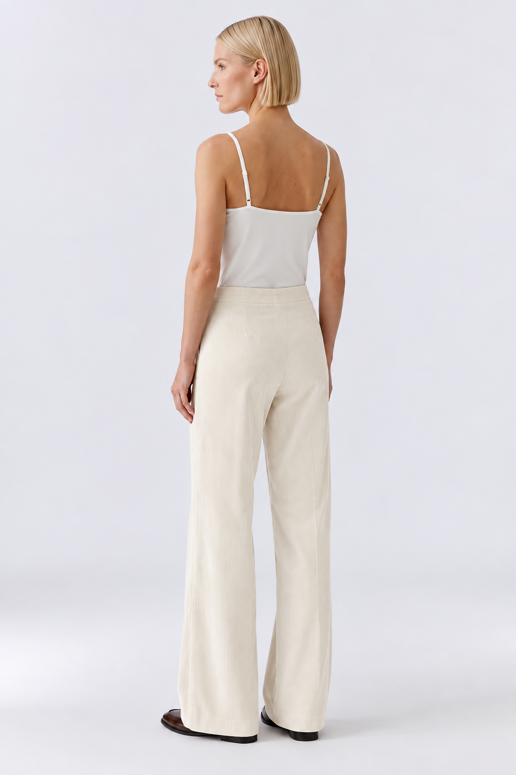 A woman shown from the back wearing a light cream camisole top and matching wide-leg trousers, photographed against a clean light gray studio background.