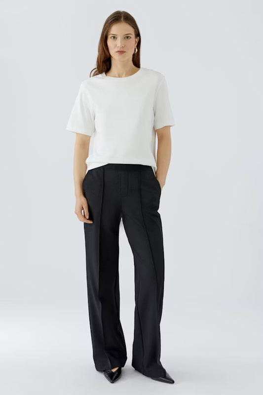 Woman wearing a white top and black pants on a light gray background