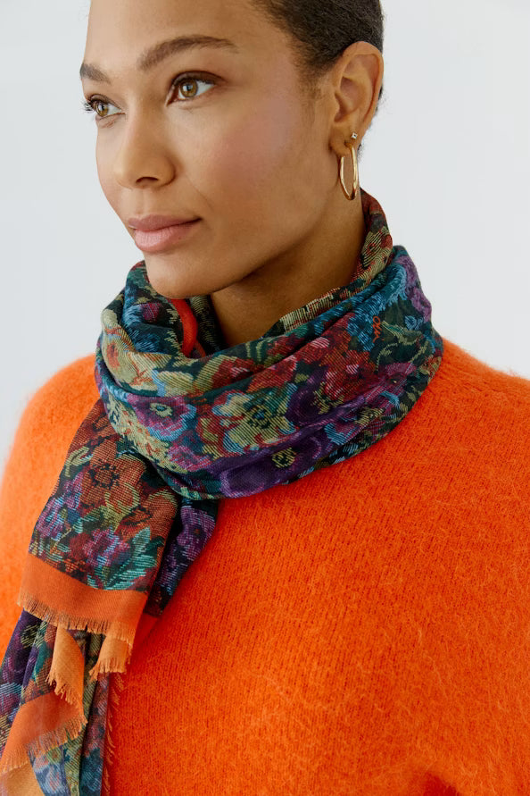 Woman wearing a colorful floral scarf and orange sweater on a white background