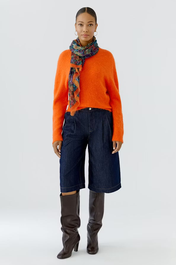Person wearing an orange sweater, blue pants, and brown knee-high boots with a colorful scarf on a white background