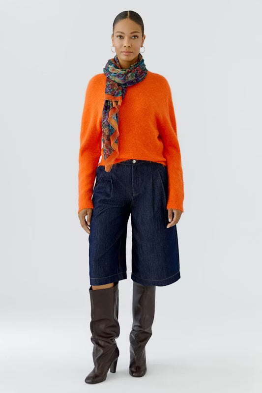 Person wearing an orange sweater, blue pants, and brown knee-high boots with a colorful scarf on a white background