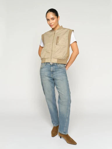 Woman wearing a beige vest, white shirt, blue jeans, and brown boots on a white background