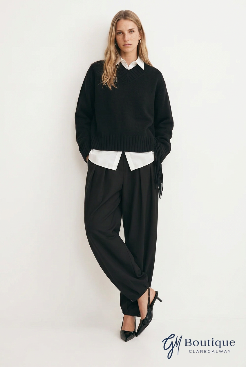 A woman models a black knit sweater vest over a white collared shirt, paired with black wide-leg trousers and black pointed heels, against a plain white studio background. A 'GM Boutique Claregalway' logo is visible in the bottom right corner.