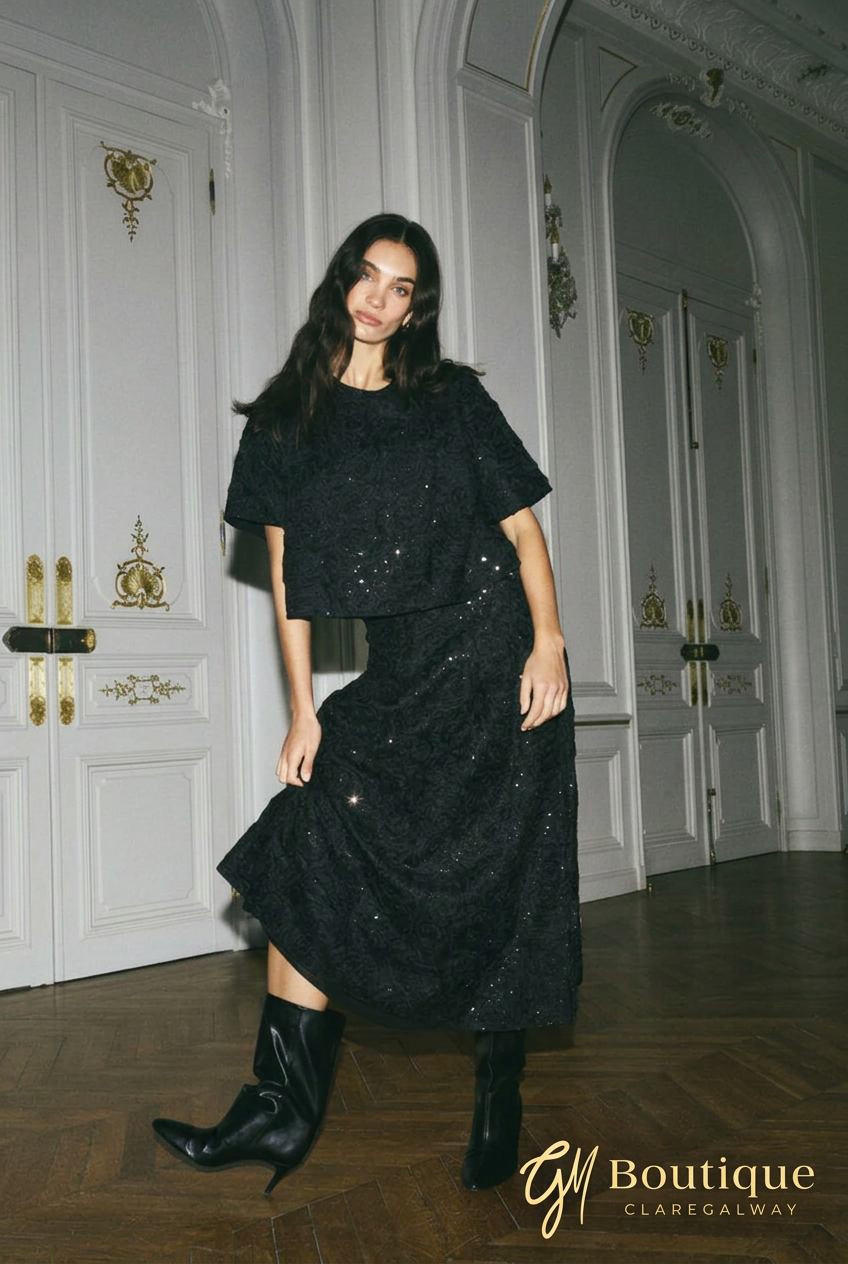 Model wearing Mos Mosh Reya black short-sleeve sequin top with the matching skirt and black boots.