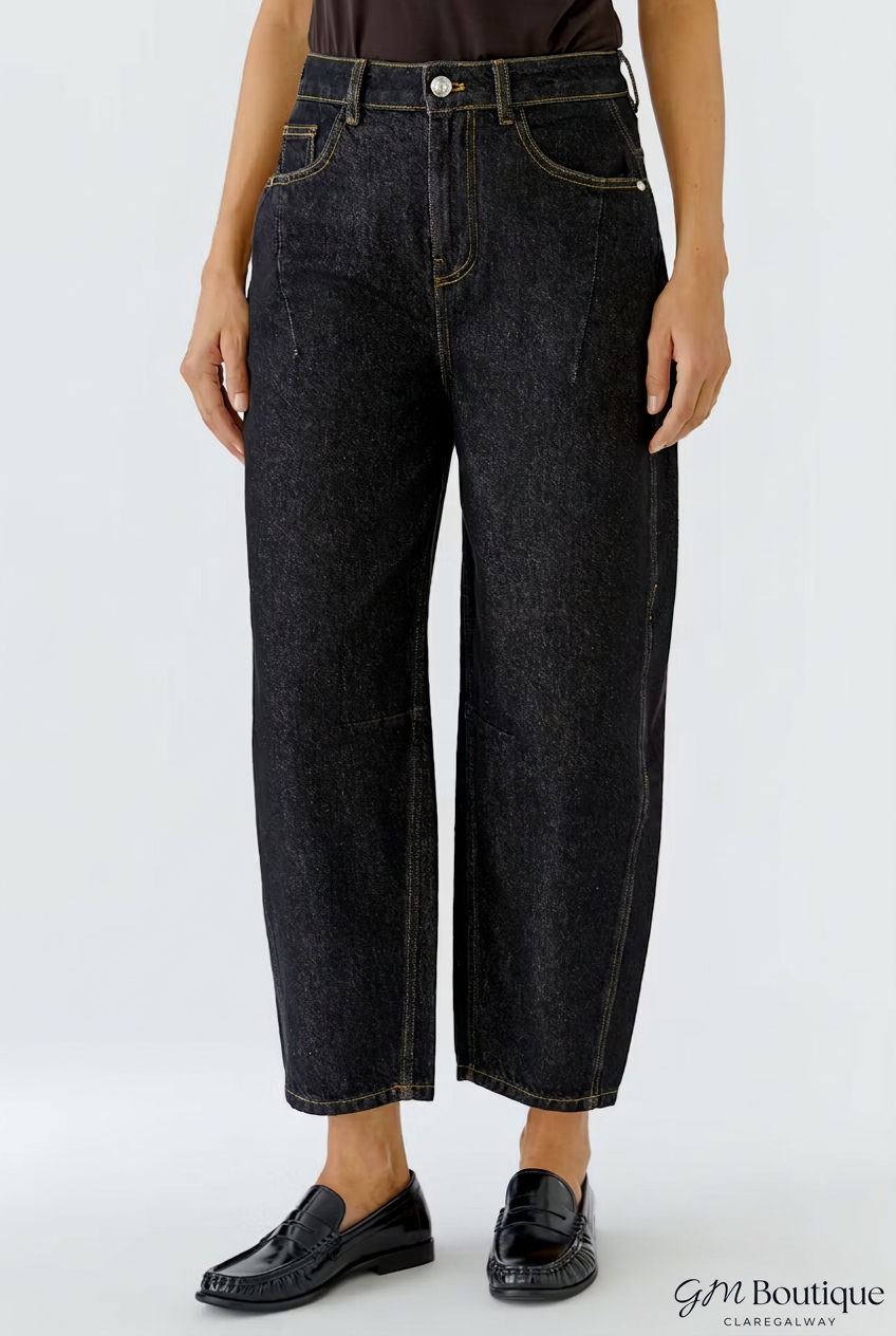 A model wearing a pair of dark wash cropped jeans with a straight-leg fit, paired with black leather loafers, shown from the waist down on a light gray background.