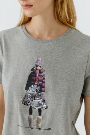 A close-up of a woman wearing a heather gray Oui crewneck t-shirt with a detailed graphic print of a woman in winter clothing on the front. GM Boutique | Galway