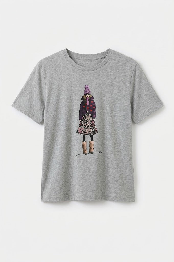 A heather gray short-sleeve crewneck t-shirt featuring a central graphic illustration of a child wearing a purple hat and a patterned coat, displayed against a clean white background. GMBoutique | Galway