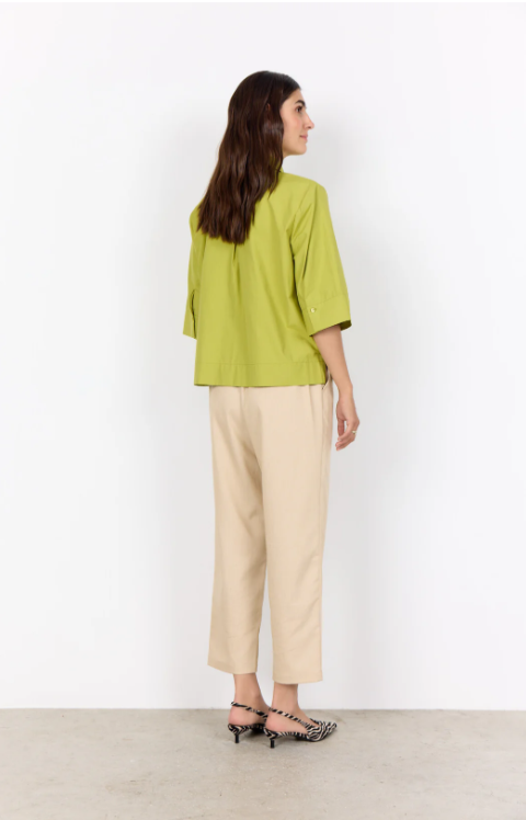 Woman wearing a green top and beige pants against a white background