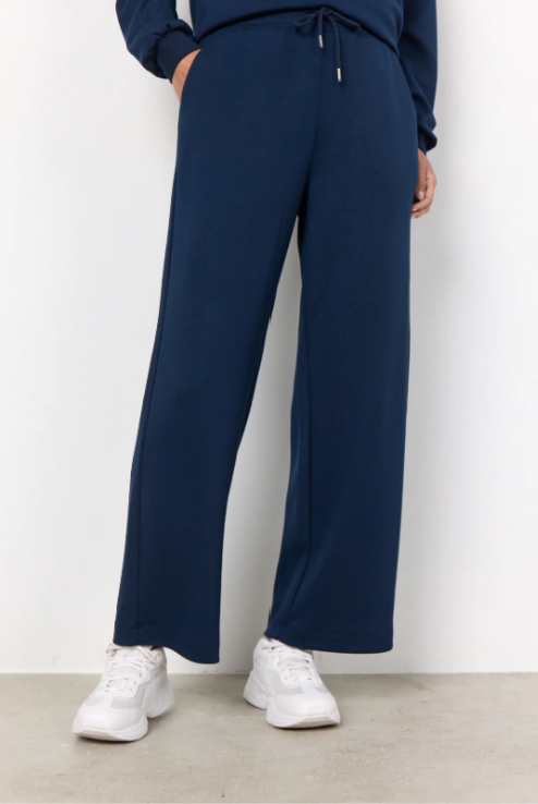 Person wearing navy blue pants and white sneakers on a plain background