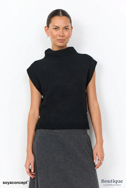 A woman modeling a black sleeveless ribbed mock-neck knit top paired with a dark gray skirt, photographed against a clean white studio background.