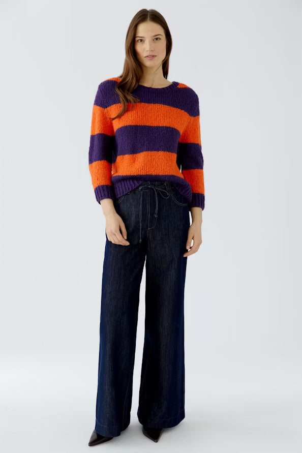 Person wearing a colorful striped sweater and dark pants on a white background