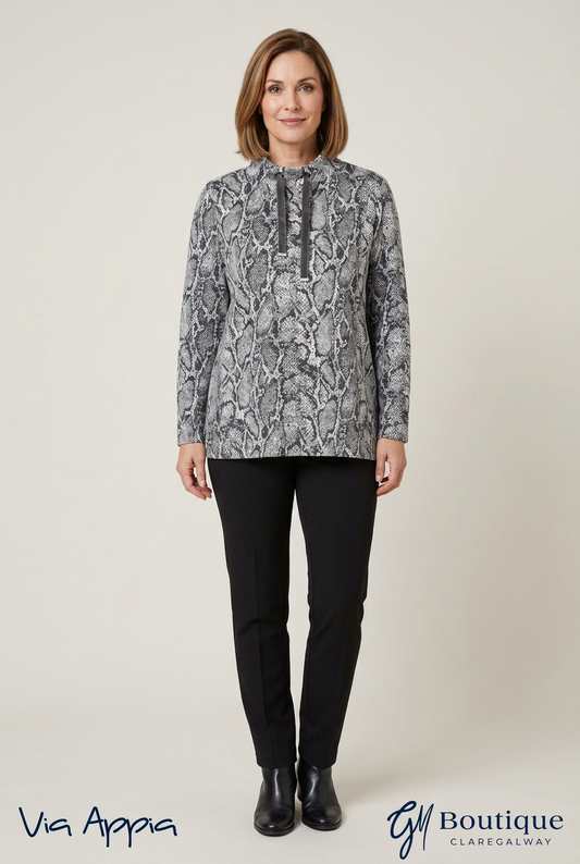 A woman modeling a long-sleeve high-neck top with a gray and white abstract pattern, paired with black trousers and black boots, against a light beige studio background. Brand logos 'Via Appia' and 'Boutique Claregalway' are visible at the bottom.