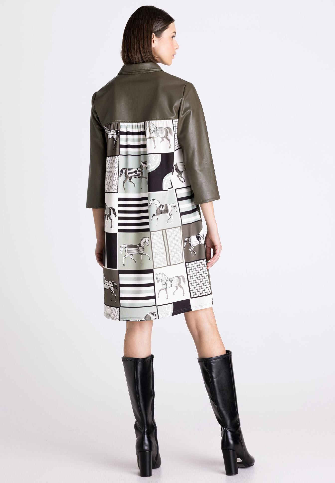 A model from the back wearing a short olive green faux-leather jacket with a patchwork print panel on the back in black, white, and gray, paired with black knee-high boots, against a light gray studio background.