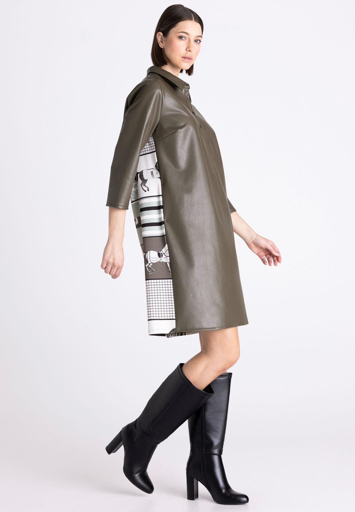 A model wearing an olive green faux-leather coat with a black and white patterned scarf draped over one side, paired with black knee-high leather boots, against a light gray studio background.