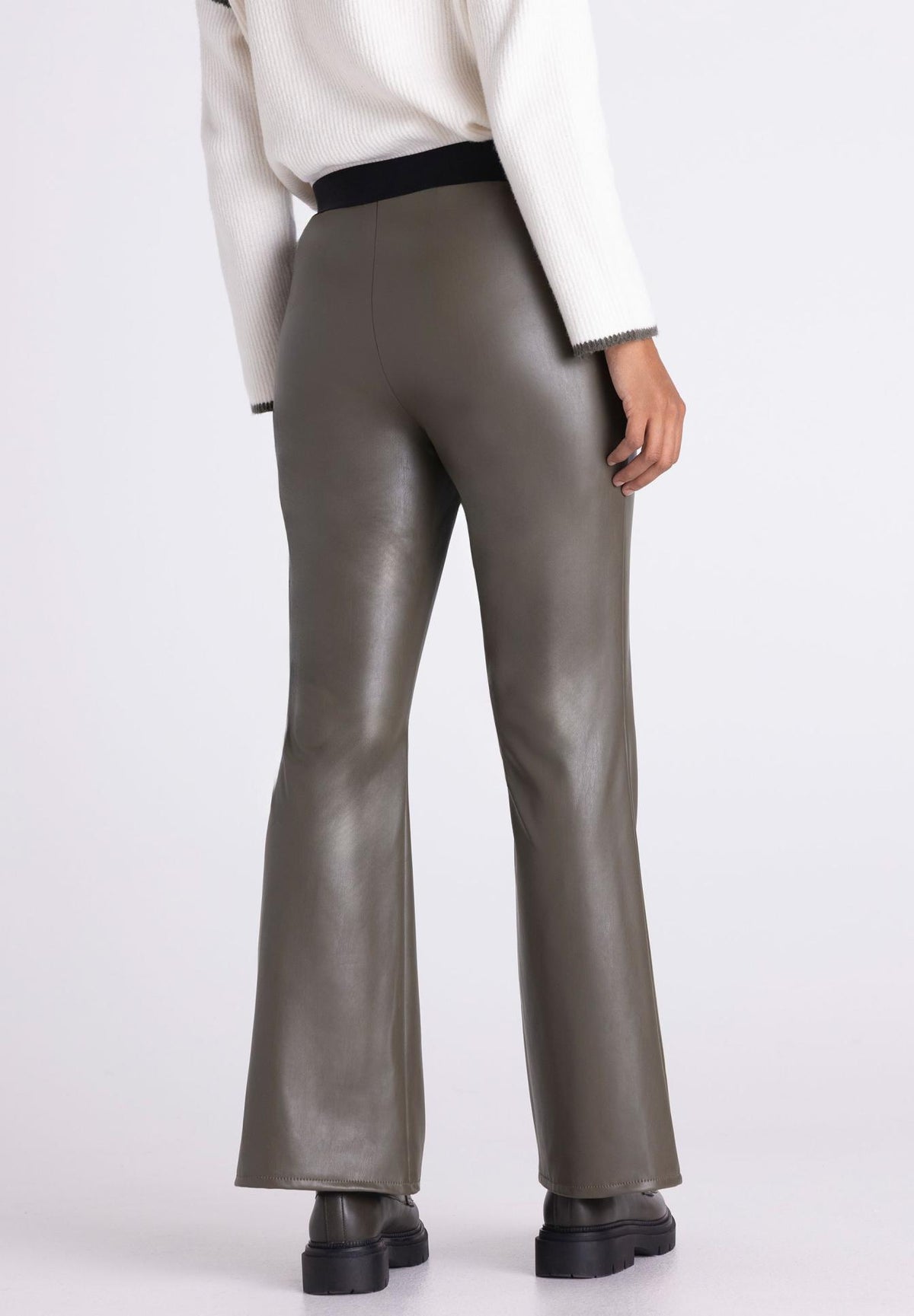 A person shown from the back wearing high-waisted, flared pants in a smooth taupe-brown material, paired with a cream top and black shoes, against a light gray studio background.