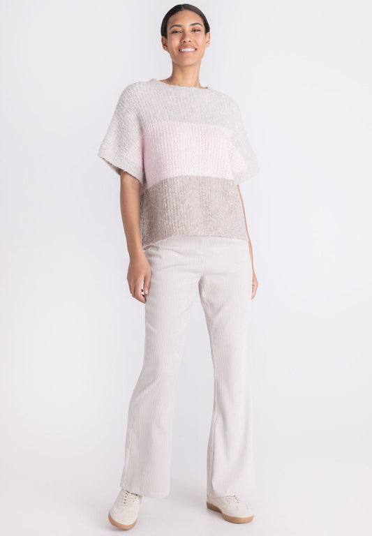 A woman modeling a short-sleeve knit top with horizontal color-blocked stripes in light gray, pale pink, and taupe-beige, paired with light beige pants and white sneakers against a plain white studio background.