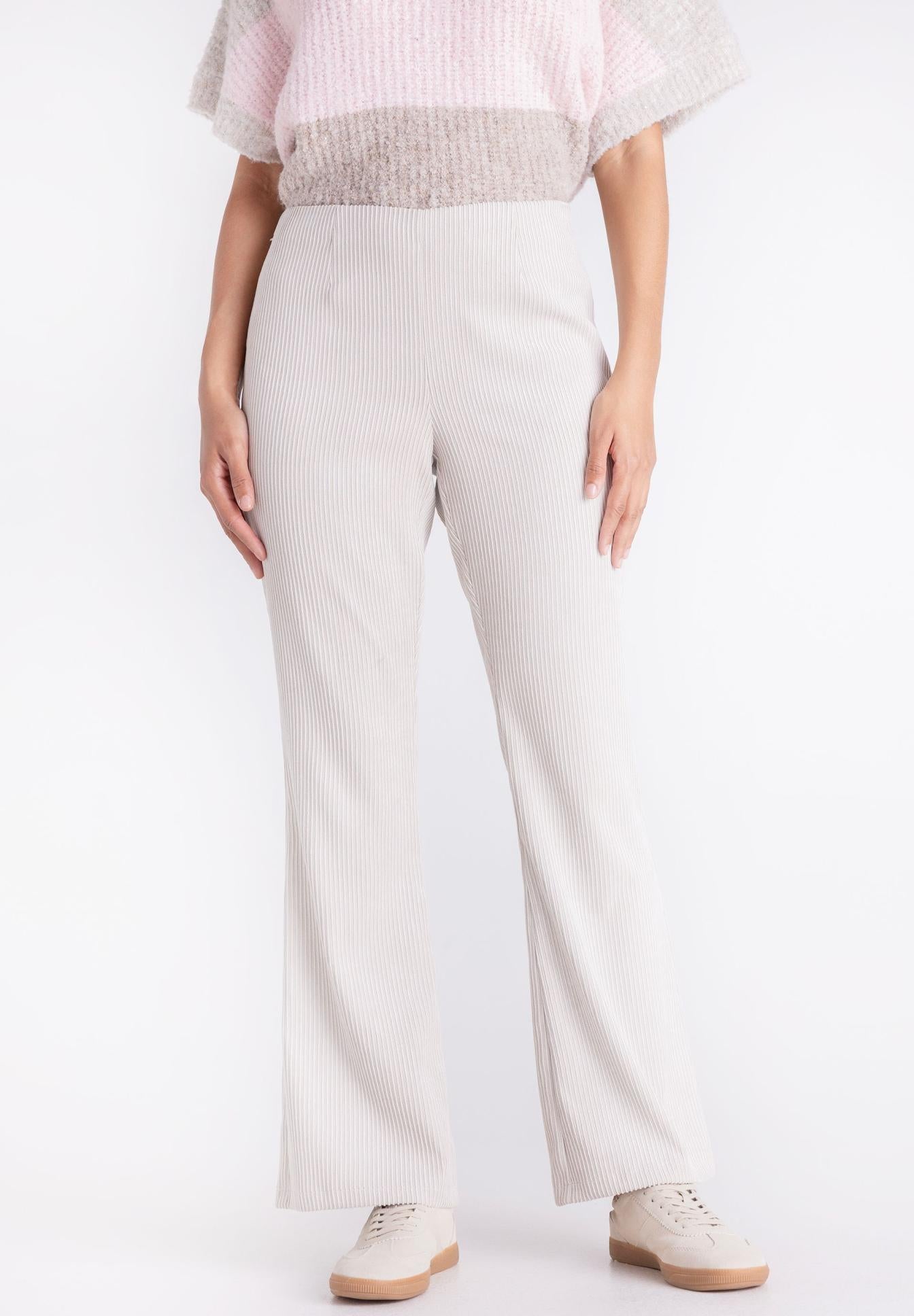 A model is wearing light beige wide-leg trousers with a subtle vertical ribbed texture, paired with a pink and beige top and beige sneakers, set against a plain white studio background.